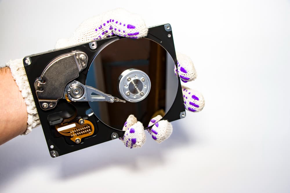 A hand holding a hard drive with purple gloves.