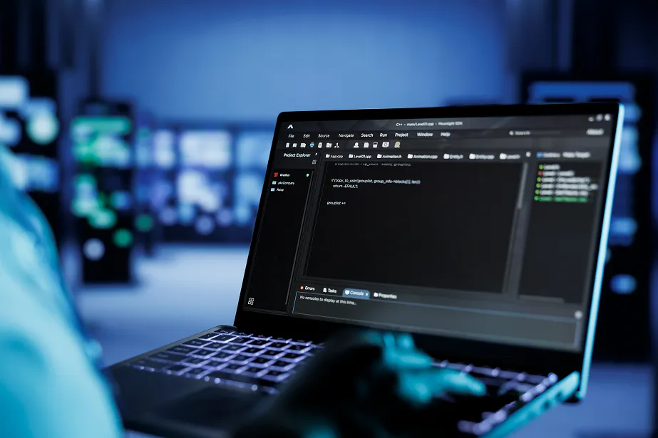 A person using a laptop with code editor software open on the screen in a dark, high-tech environment